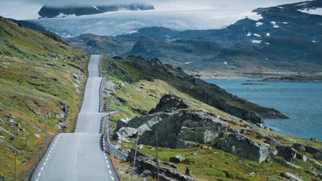 Eine-Schmale-Bergstraße-Sognefjellsvegen-Schlängelt-Sich-Durch-Eine-Felsige-Landschaft,-Ein-Gletscher-Dominiert-Den-Hintergrund