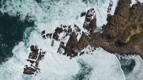 Aerial-birds-eye-view-showcasing-powerful-ocean-waves-crashing-against-the-rocky-coastline-at-Playa-Chica,-Quintay-in-Valparaíso,-Chile