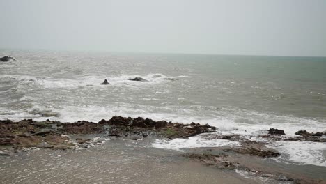 Waves-crash-on-a-rocky-shoreline-under-an-overcast-sky,-creating-a-peaceful-coastal-scene