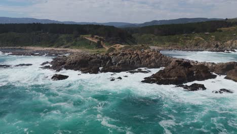 Aerial-view-of-powerful-ocean-waves-crashing-on-the-rocky-coastline-of-Quintay,-Valparaíso,-Chile,-showcasing-the-stunning-natural-beauty-and-rugged-landscape-of-the-region