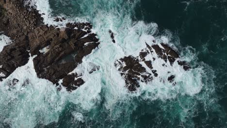 Aerial-birds-eye-view-showcases-the-rugged-rocky-outcrop-surrounded-by-crashing-waves-at-Playa-Chica,-located-in-Quintay,-Casablanca,-Valparaíso,-Chile