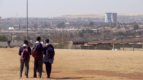 Teenage-school-students-walking-home-through-open-park-with-a-backdrop-of-Soweto-township-and-the-landmark-cooling-towers