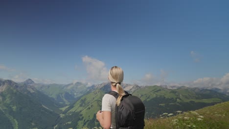 A-woman-hikes-through-the-scenic-Austrian-Alps,-taking-in-mountain-views-under-a-bright-sky