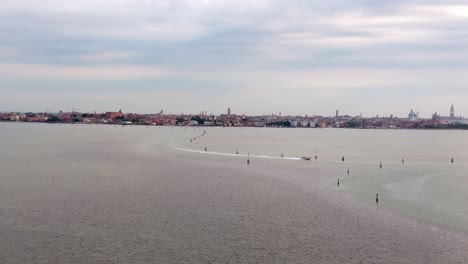 Aerial-Flyover-Of-A-Boat-Cruising-On-A-Bay-With-The-Venice-Skyline-On-The-Horizon,-Italy