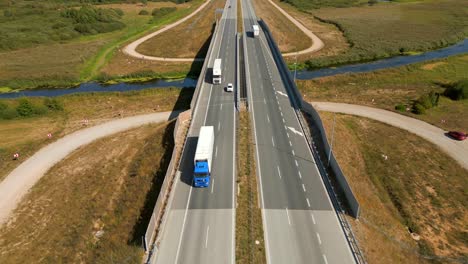 Trucks-driving-on-the-highway-through-rural-forested-landscape,-Aerial-view