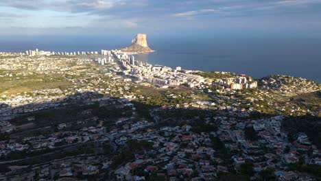 Calpe-and-penyon-d'ifach-rock-on-a-sunny-day-with-sea-and-cityscape-backdrop,-aerial-view