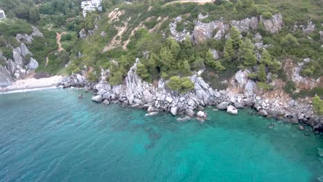 Aerial-view-of-small-beach-with-turquoise-water-next-to-rocks-and-trees-in-the-area-of-Agia-Paraskevi-Halkidiki,-Greece