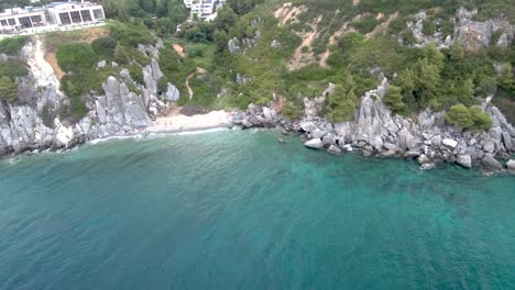 Aerial-view-of-the-small-turquoise-beach-with-rocks,-under-a-hot-Springs-building,-in-the-area-of-Agia-Paraskevi,-Halkidiki,sideways-movement-by-drone