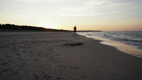 Hombre-Corriendo-En-La-Playa-En-El-Mar-Báltico-Durante-La-Puesta-De-Sol-En-Swinoujscie,-Polonia