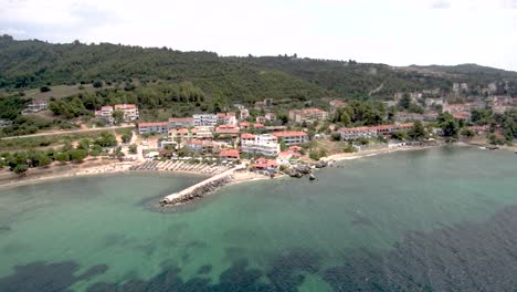 Aerial-view-of-small-beach-with-rocks-under-a-tourist-village-in-the-area-of-Agia-Paraskevi-Halkidiki,-Greece-,sideways-movement-by-drone