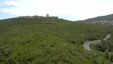 Aerial-shot-of-a-hill-next-to-a-provincial-road-with-a-castle-on-its-top