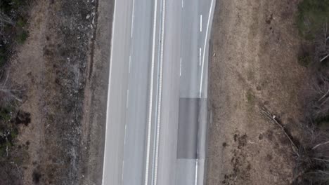 Top-down-drone-shot-of-highway-going-through-Swedish-forest-in-early-autumn