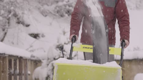 Slow-motion-footage-of-a-person-pushing-a-yellow-snowblower-clearing-a-snowy-driveway