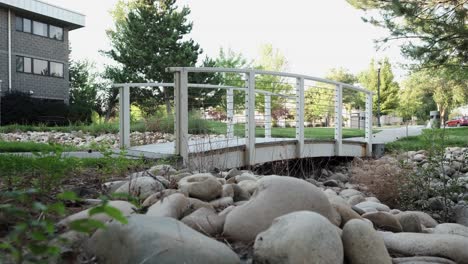 Idyllic-White-walking-bridge-in-small-outdoor-park-with-autumn-trees-and-white-stones---static