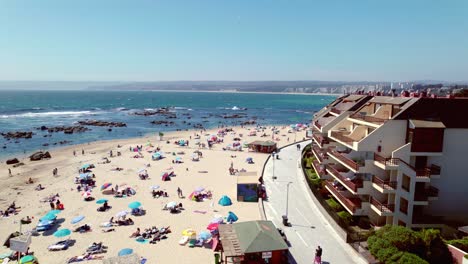 Aerial-Drone-Fly-Above-White-Sand-Beach-and-Pristine-Blue-Sea-Water-of-Pejerrey-Algarrobo,-People-relaxing-at-Chile-Travel-and-Tourism-Summer-Destination