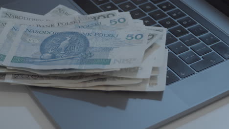Man-counts-Polish-money,-puts-banknotes-in-pile-stacked-on-laptop-keyboard