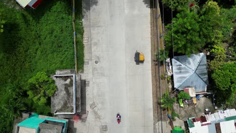 Top-down-aerial-pan-across-bustling-street-in-southeast-asia-village-in-countryside,-mopeds-driving