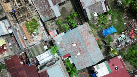 Birdseye-view-aerial-pan-across-rusted,-half-built,-ramshackle-roofs-and-busy-street