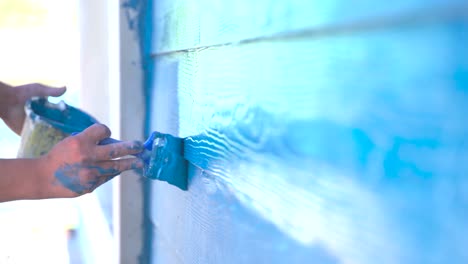 A-closeup-shot-of-a-man-hand-painting-the-wooden-walls-with-blue