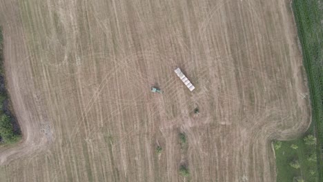 Aerial-top-shot-of-a-tractor-depositing-a-hay-bale-in-a-field-in-France