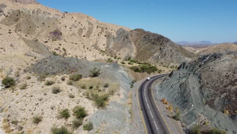 Aerial-drone-forward-moving-shot-flying-over-car-and-truck-driving-along-the-winding-RCD-Road-surrounded-by-arid-vegetation-in-Balochistan-on-a-sunny-day
