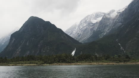 Un-Viaje-Panorámico-A-Lo-Largo-De-Un-Fiordo-Con-Hermosas-Cascadas-Y-Montañas-Cubiertas-De-Nieve-En-El-Fondo