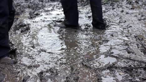 Two-young-children-playing-in-a-muddy-puddle,-wearing-waterproof-clothing