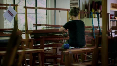 Woman-sits-at-sewing-loom-working-with-hands-to-prepare-and-tie-knots,-cinematic