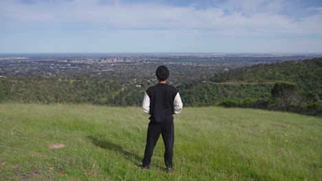 Back-View-Of-An-Indian-Punjabi-Sikh-Man-Looking-At-The-Beautiful-View-Of-Green-Mountain,-Forest,-And-City