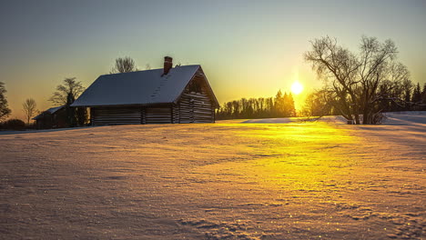 Snowy-landscape-with-a-wooden-house-or-cabin-under-the-golden-sky-at-sunset