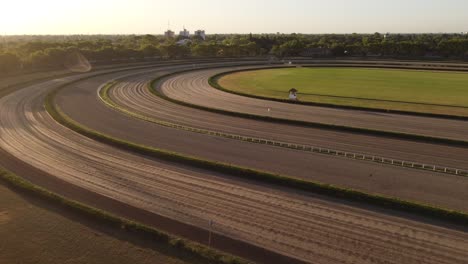 Aerial-forward-flight-over-empty-horse-racecourse-during-golden-sunset-in-Buenos-Aires,Argentina---Surrounded-by-green-forest-woodland