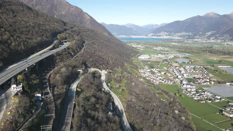 Aerial-View-of-Highway-and-Railroad-Above-Valley-and-Small-Town-by-Lake-in-Swiss-Alps-on-Sunny-Spring-Day