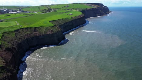 aerial-view-of-long-coastline-showing-tall-cliffs-and-multiple-coves-and-textures-as-waves-crashing-from-the-ocean-into-the-cliffside-with-birds-flying-around