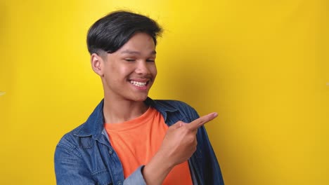Young-asian-man-in-casual-style-pointing-finger-to-the-side-showing-space-for-advertisement,-promotion-and-sale,-isolated-on-yellow-background