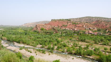 Rural-village-in-valley-with-lush-vegetation-and-river-in-Morocco,-high-angle