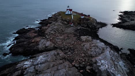 Flyover-and-uptilt-over-lighthouse-on-a-rocky-island-with-tidal-water-crashing-on-rocks-and-a-soft-sunset