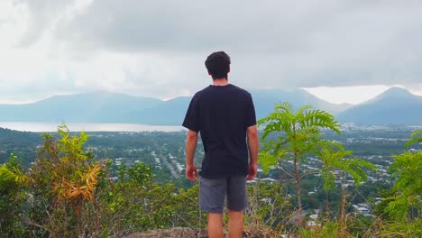 Man-approached-peaceful-lookout-of-cairns-in-australia,-mountains-in-the-background-are-covered-by-clouds-and-hiding-the-morning-sun