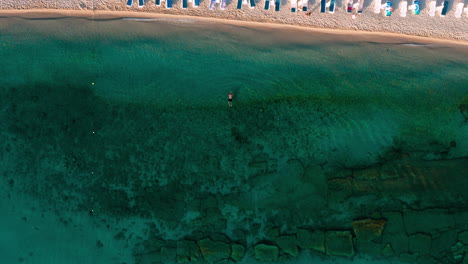 Top-down-view-of-beach-with-umbrellas-in-Hanioti-,-Greece-and-swimming-man