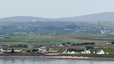 Telephoto-lens-shot-of-Stornoway-and-a-nearby-wind-farm-with-active,-spinning-wind-turbines