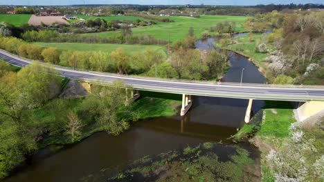 Drone-Slow-Dolly-Shot-Forward-Old-Bridge-in-Łęczna,-Poland-with-Cars,-River,-and-Green-Nature