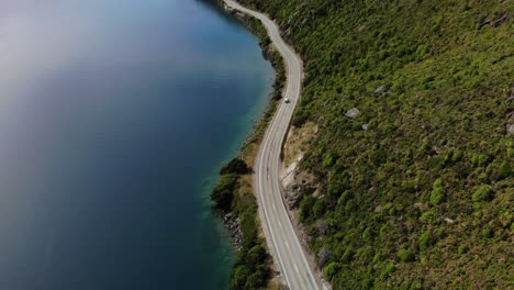 Car-driving-on-winding-road-reveal-of-beautiful-New-Zealand-landscape,-aerial-tracking