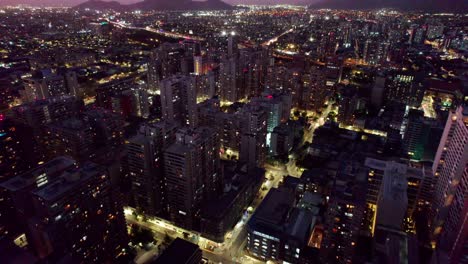 Beleuchtete-Futuristische-Nächtliche-Hochhaus-Stadtansicht-Von-Santiago,-Chile,-Luftaufnahme,-Die-über-Verschiedene-Alte-Und-Moderne-Wolkenkratzerhauptstädte-Fliegt