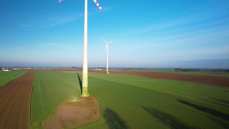 Aerial-ascending-over-Spinning-Wind-Turbines-in-Green-Agricultural-Fields-on-Sunny-Day-with-Cloudless-Sky