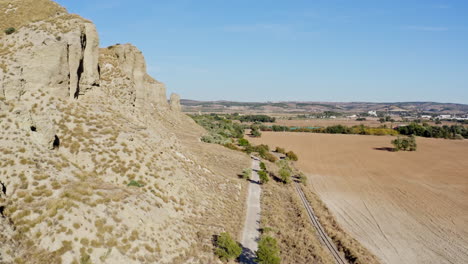 Solo-cyclist-on-a-long-gravel-road-in-dry-countryside-in-Madrid,-Spain,-aerial
