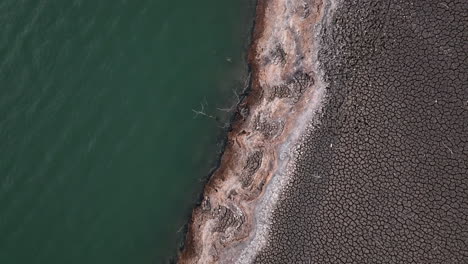 Dramatic-aerial-shot-of-dry-cracked-soil-along-Sau-swamp-shores,-Catalonia-in-Spain
