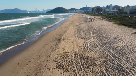 Drone-shot-of-praia-Brava-in-Brazil,-with-people-and-the-city-in-the-background