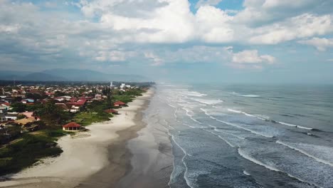 Descending-aerial-shot-of-Brazilian-beach-in-summer-time-with-big-waves,-sand-and-clouds