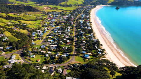 Aerial-reveal-of-holiday-houses-beside-beautiful-white-sand-beach,-Whangapoua,-New-Zealand