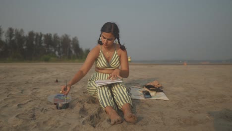 Die-Schöne-Indische-Frau-Malt-Gerne-Kunst-Auf-Ihrem-Schoß-Am-Strand