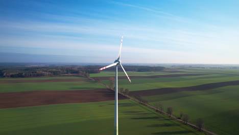 Static-drone-shot-of-windmill-rotating-on-rural-green-and-brown-cultivation-fields-of-Poland
